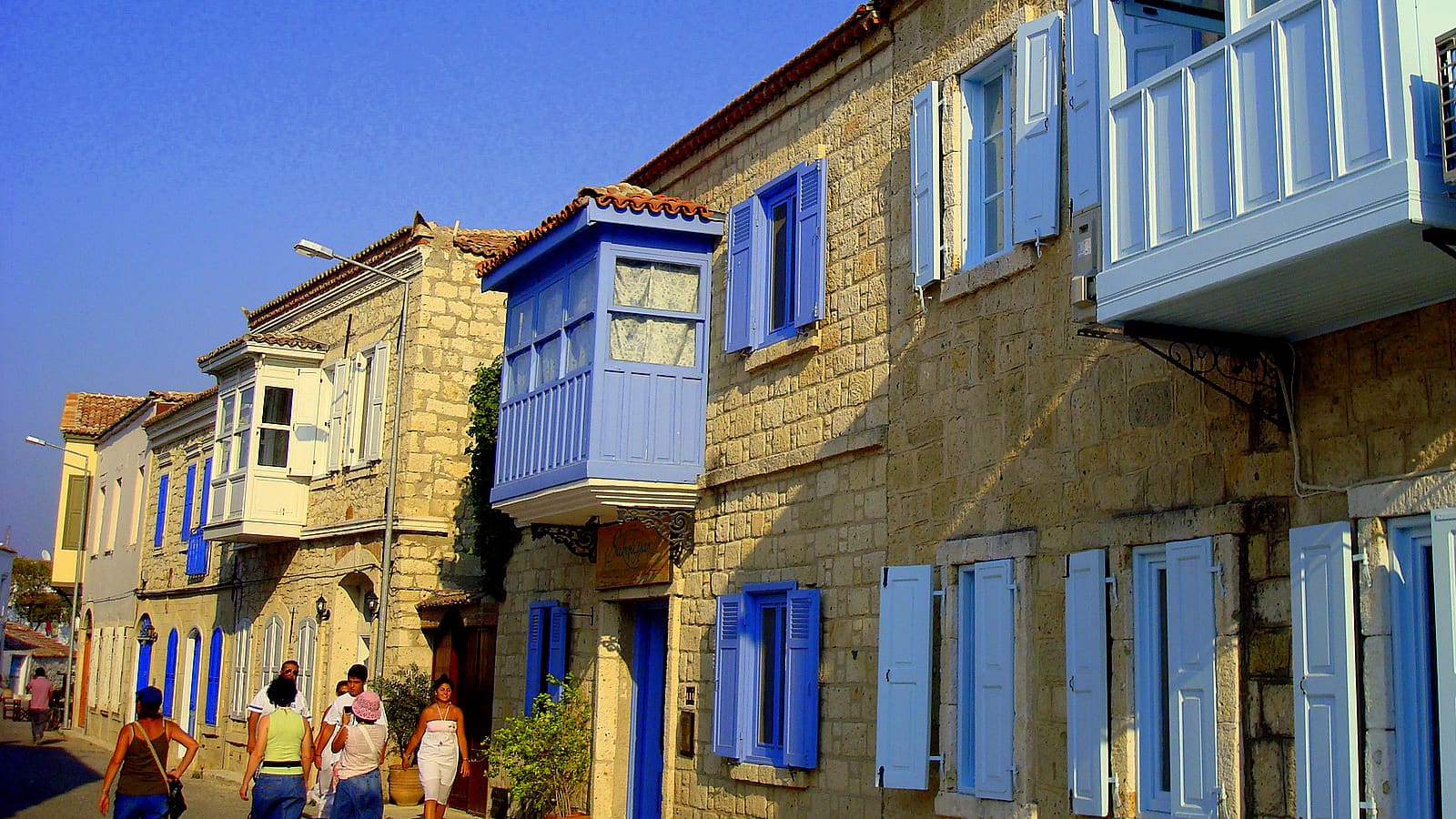 Stone houses with blue shutters on a narrow street in Çeşme